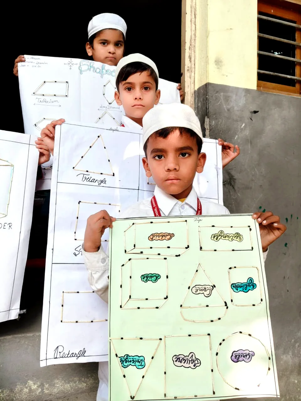 Students hold up their schoolwork and drawings.